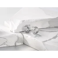 Silver hoop earrings with triple-band design displayed on white marble surfaces and draped fabric.