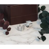 Three silver rings displayed on white marble surrounded by a brown box and dried eucalyptus stems in burgundy and green tones.