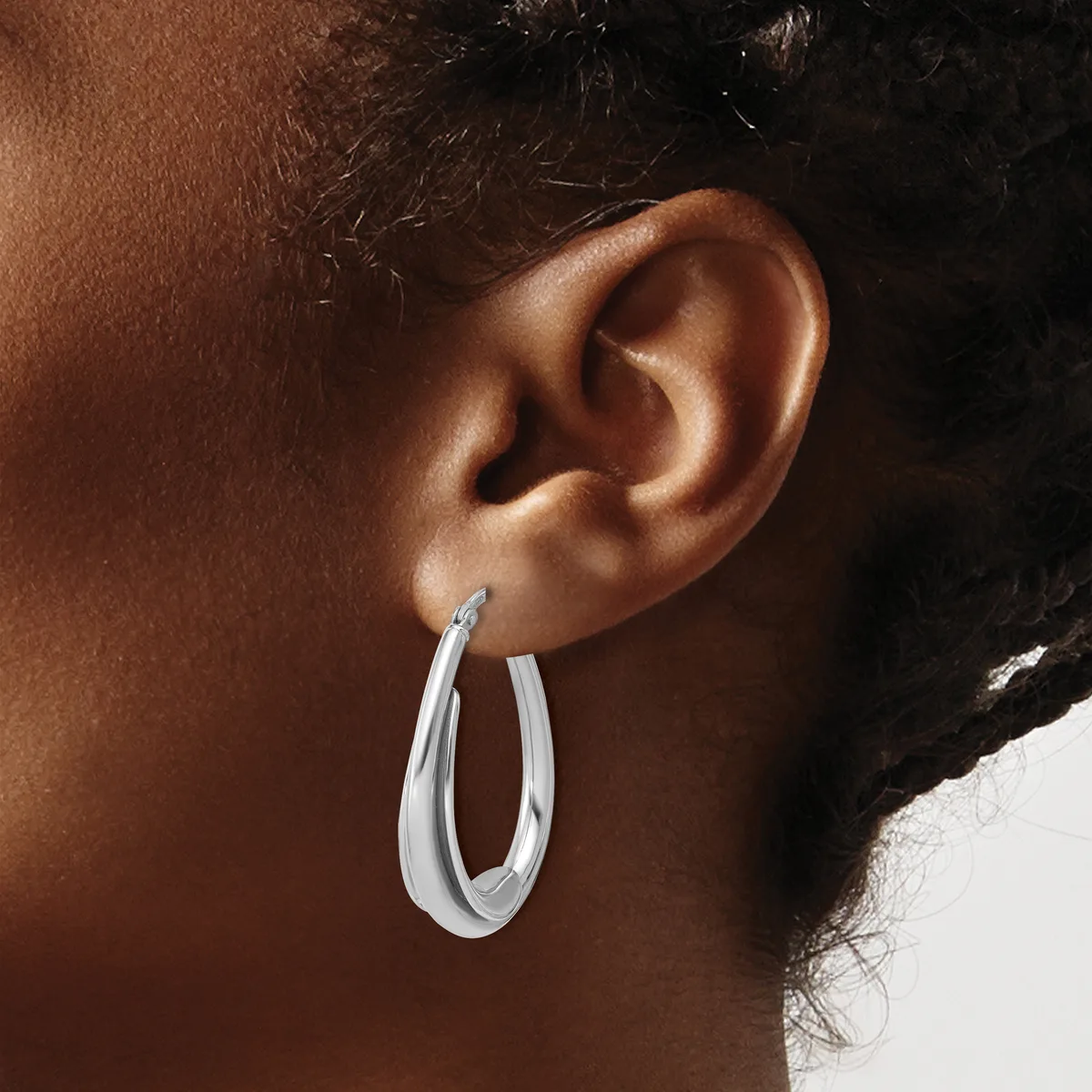 A person wearing a pair of polished silver hoop earrings with a curved, tapered design shown in profile against their ear.