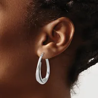 A person wearing a pair of polished silver hoop earrings with a curved, tapered design shown in profile against their ear.