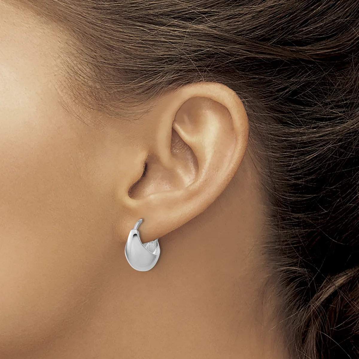 A woman wearing a small polished silver crescent-shaped hoop earring in her earlobe, shown from the side profile.