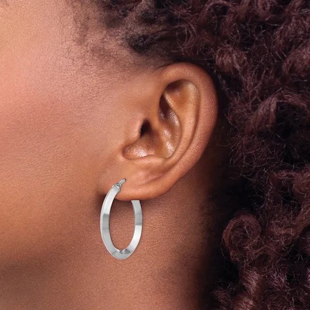 A person wearing a pair of polished silver oval hoop earrings, shown from the side view of their ear and neck.