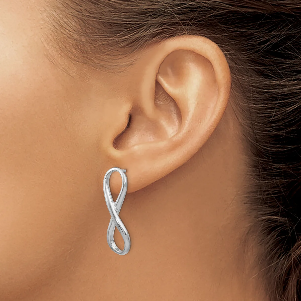 A silver infinity symbol earring worn in a person's earlobe, shown from a side profile view.