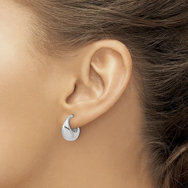 A person wearing a polished silver chunky curved hoop earring in their ear lobe.
