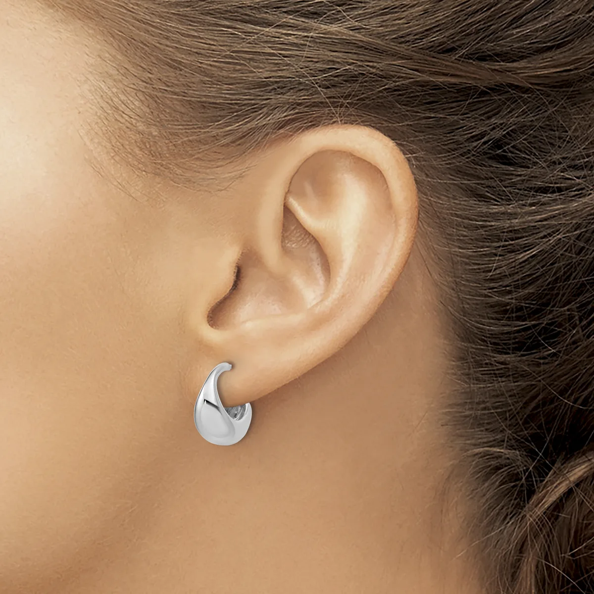 A person wearing a polished silver chunky curved hoop earring in their ear lobe.