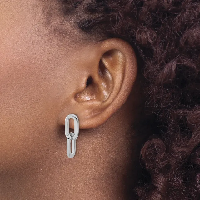 A person wearing a silver elongated oval link chain earring in their earlobe, shown in profile view against their neck and shoulder.