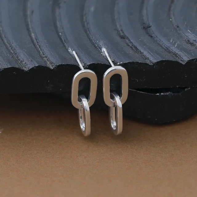Pair of silver-toned rectangular earrings with rounded corners and hanging loop closures, displayed on a textured black and gray surface.