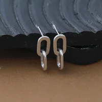 Pair of silver-toned rectangular earrings with rounded corners and hanging loop closures, displayed on a textured black and gray surface.
