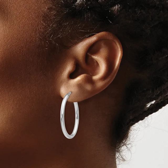 A person wearing silver hoop earrings, shown from the side profile focusing on the ear and earrings against their brown skin tone.