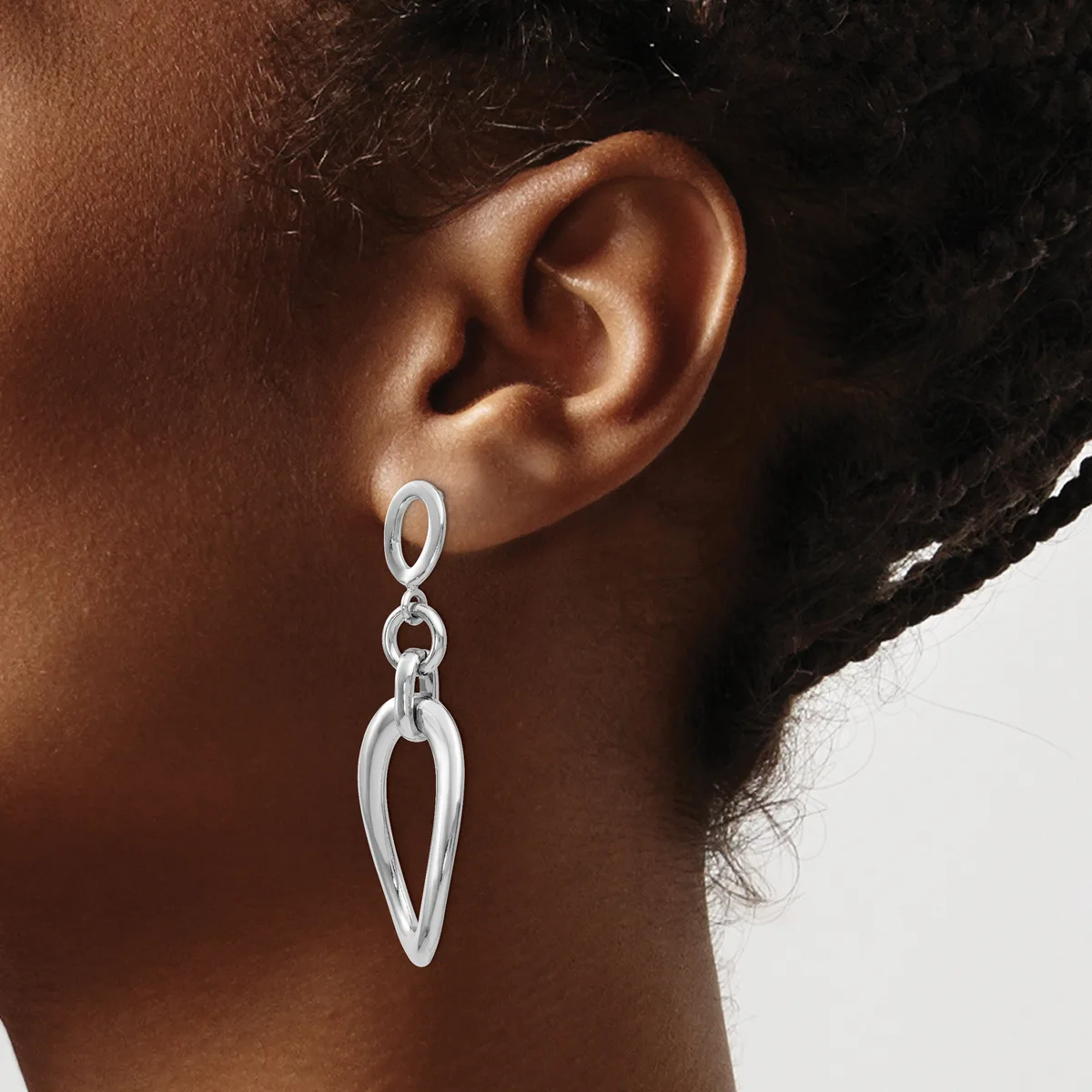A person wearing silver-toned teardrop-shaped drop earrings with an open design and chain attachments.