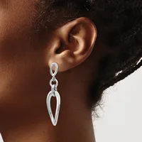 A person wearing silver-toned teardrop-shaped drop earrings with an open design and chain attachments.