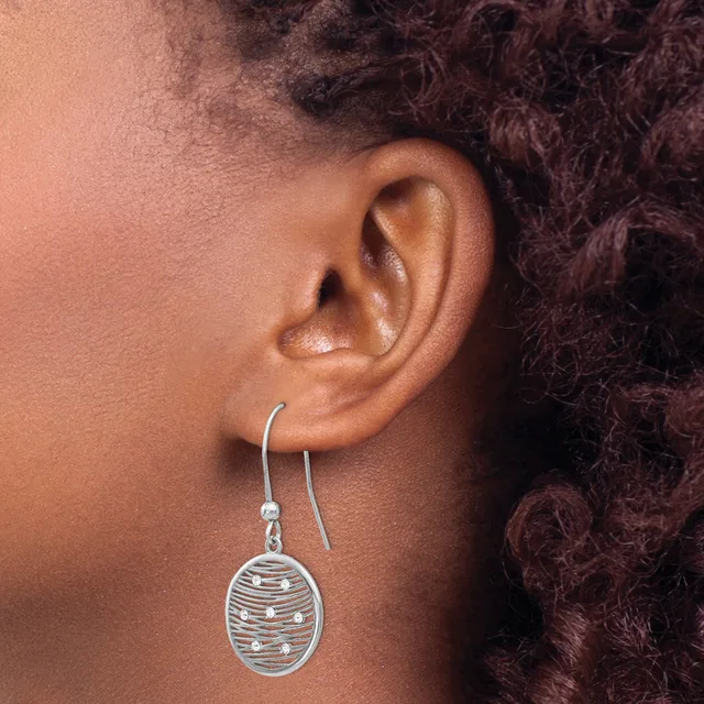 A person wearing a silver dangle earring with an oval pendant featuring horizontal striped or textured detailing, shown from the side against their ear.
