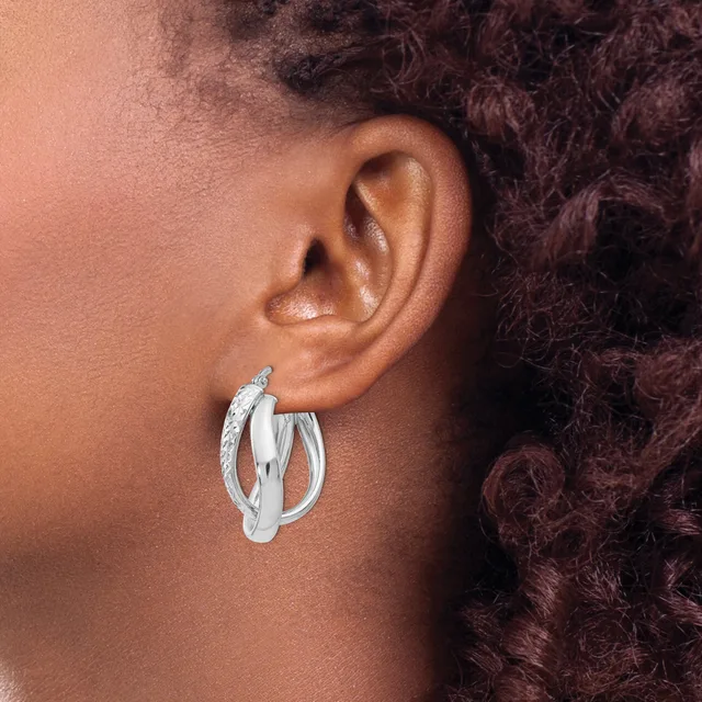 Silver hoop earrings with a textured surface worn by a person with dark curly hair, shown from the side.
