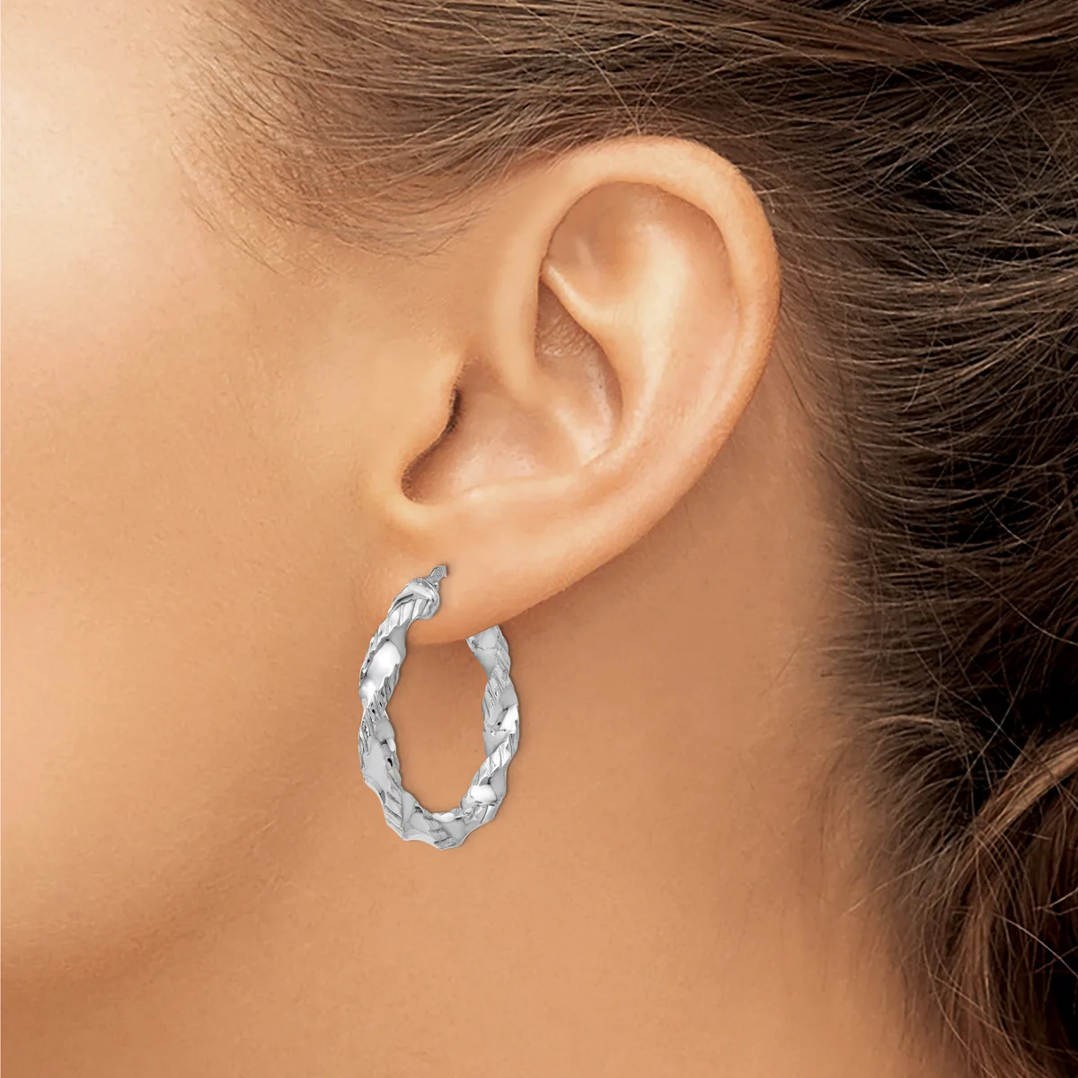 A woman wearing a twisted silver hoop earring in her earlobe, shown in profile against her neck and shoulder.