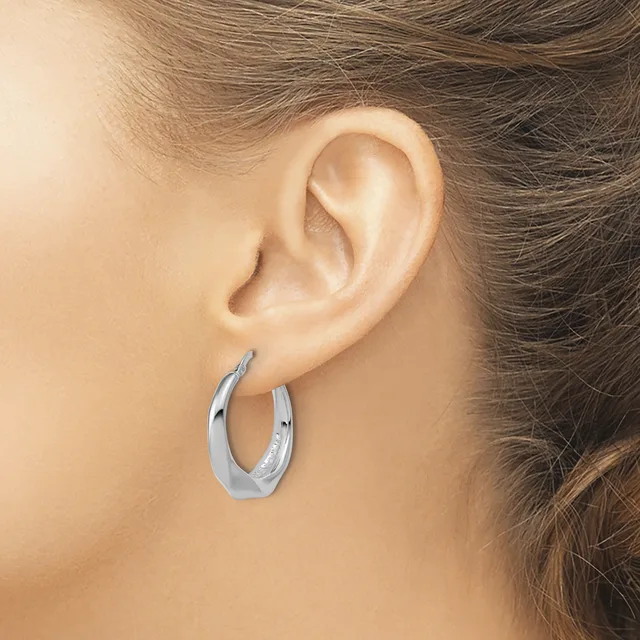 A person wearing a polished silver hoop earring with a curved, tapered design, shown from the side view of their ear.