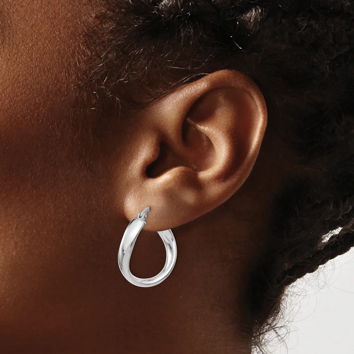 A close-up side view of a person's ear wearing a polished silver hoop earring with a smooth curved surface and small post closure.