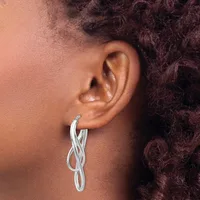 A person wearing a twisted silver hoop earring in their earlobe, shown in profile against their shoulder and dark curly hair.