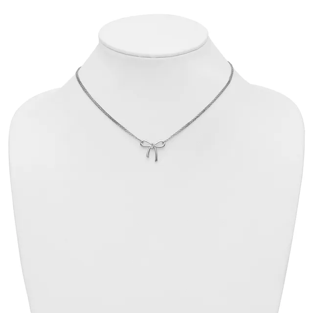 A silver-toned necklace with a delicate bow pendant displayed on a white mannequin bust.