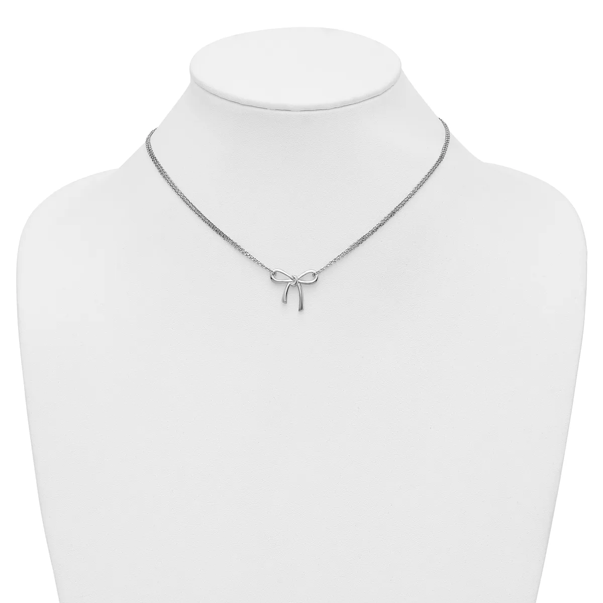 A silver-toned necklace with a delicate bow pendant displayed on a white mannequin bust.