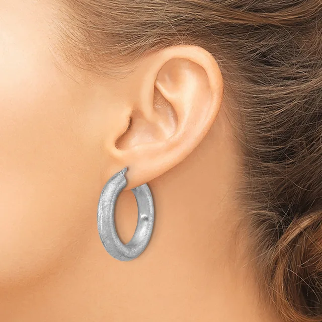 A woman wearing a pair of silver-toned hoop earrings with a brushed finish, shown from the side profile near her ear.