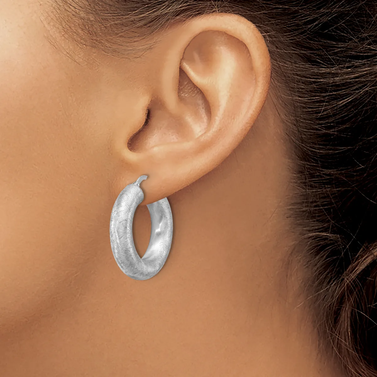 A woman wearing a pair of silver textured hoop earrings, shown from the side profile of her head and ear.