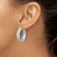 A woman wearing a pair of silver textured hoop earrings, shown from the side profile of her head and ear.