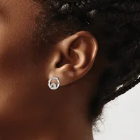 A silver circular earring with a swirl design worn in the earlobe of a person with medium brown skin and dark hair.