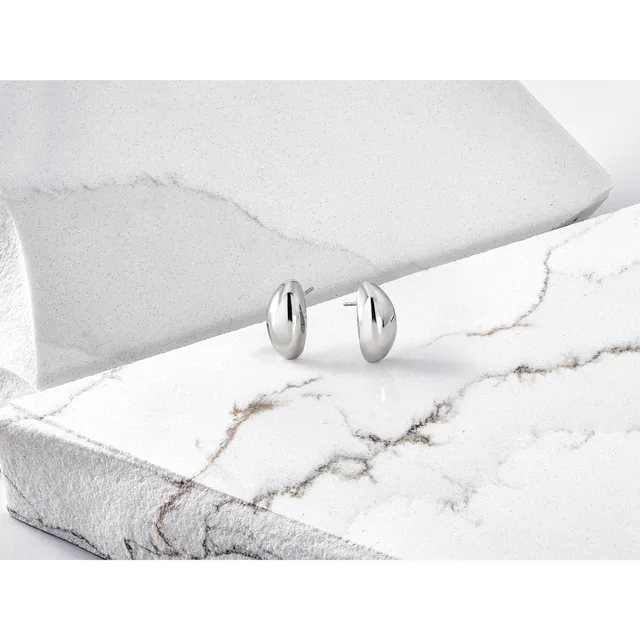 A pair of polished silver oval stud earrings displayed on white marble and stone surfaces.