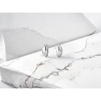 A pair of polished silver oval stud earrings displayed on white marble and stone surfaces.