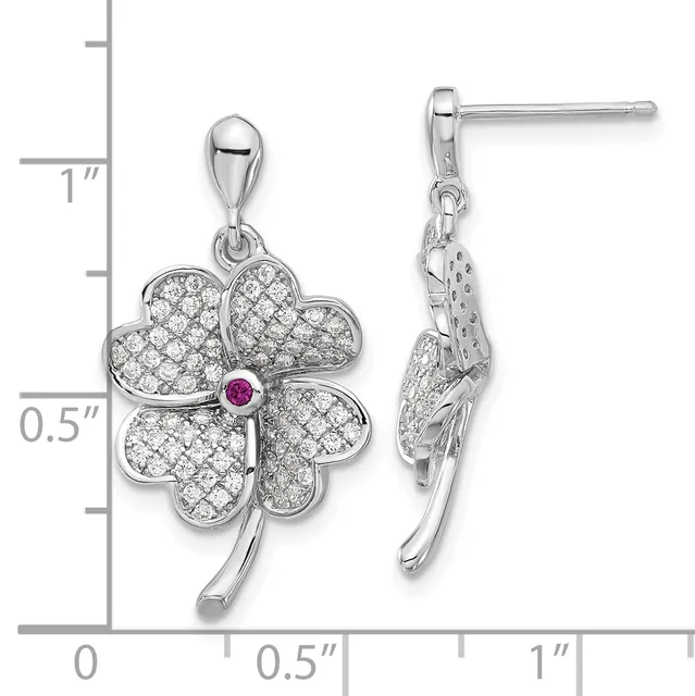 Silver four-leaf clover pendant earrings with cubic zirconia stones and a small pink ruby center stone, shown on a measurement scale.