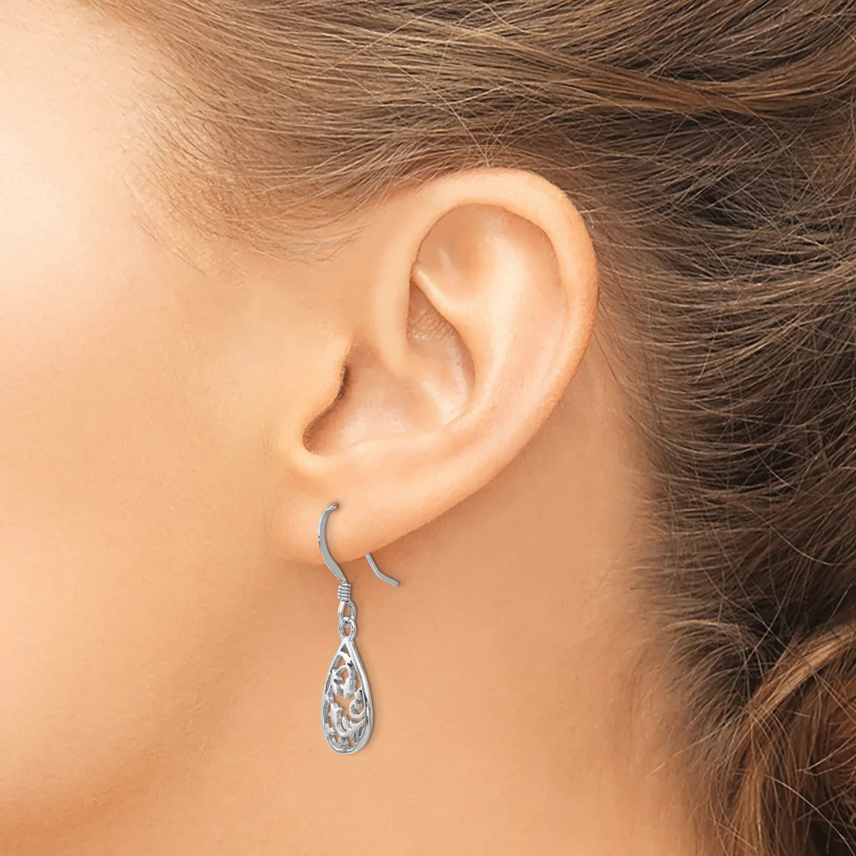 A person wearing a pair of silver teardrop earrings with ornate filigree detailing, shown from the side view of their ear and neck.