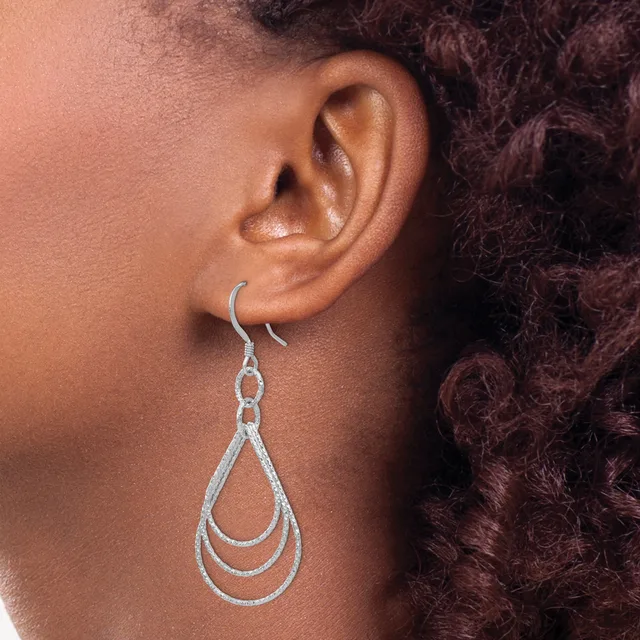 A person wearing a silver teardrop-shaped dangle earring with concentric nested loops, shown from the side against dark curly hair.