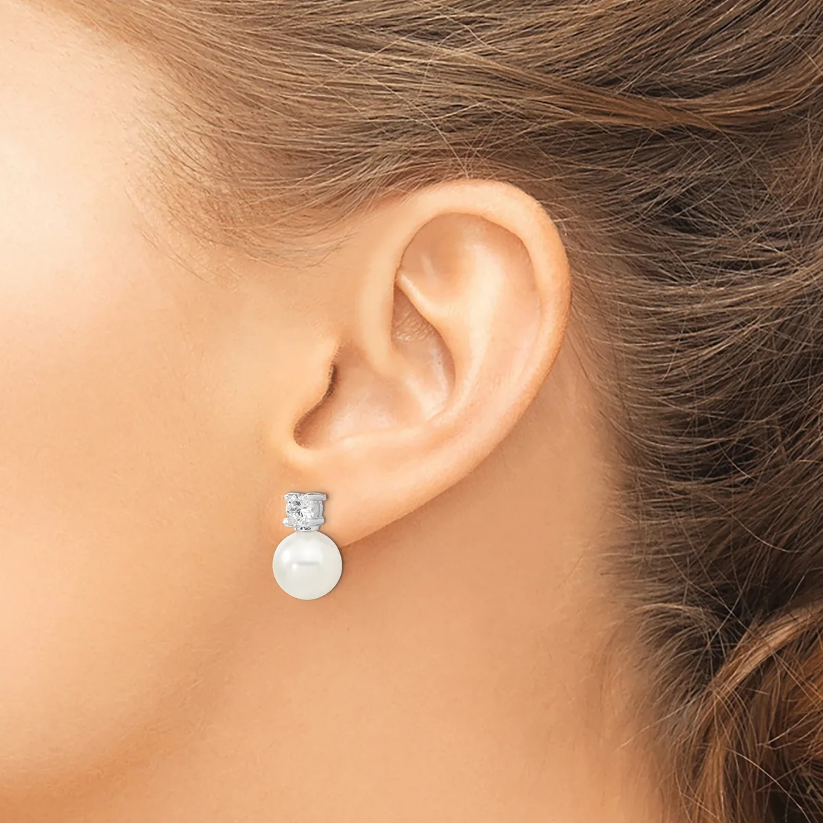 A woman wearing a pearl drop earring with a square-cut diamond or crystal stud top, shown from the side profile against her ear.