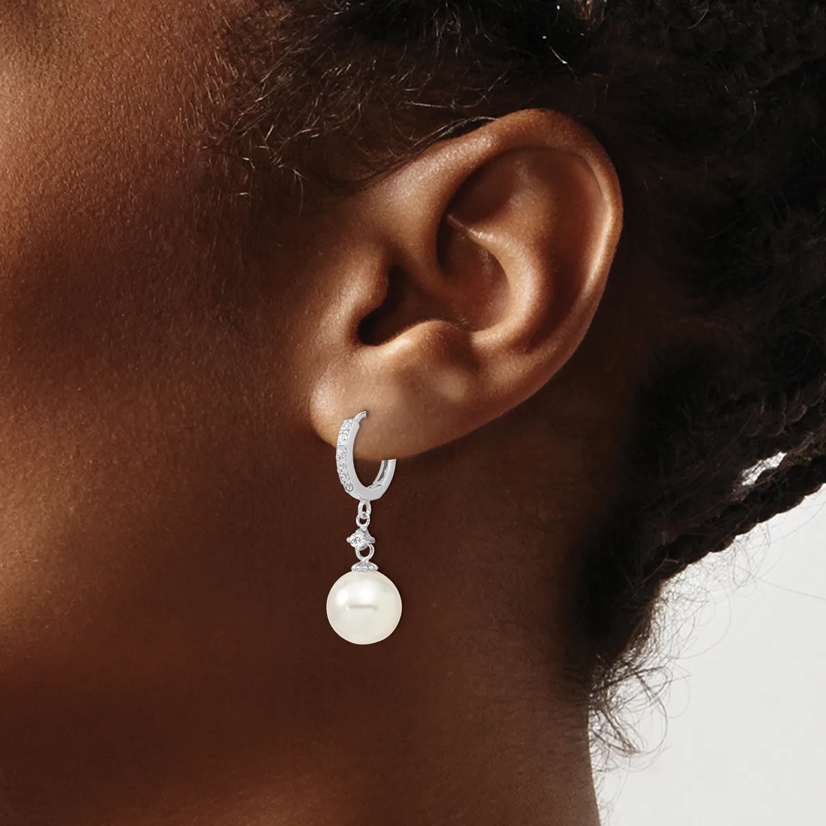 A person wearing a silver hoop earring with a dangling white pearl drop, shown from the side view of their ear and neck.