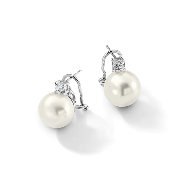 A pair of white pearl drop earrings with diamond accents and omega-style clip backs in white metal, displayed on a white surface.