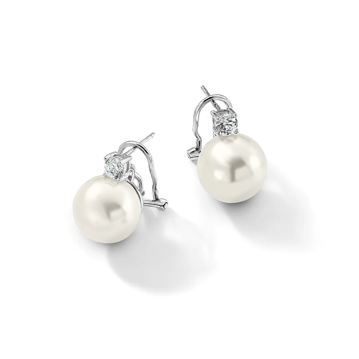 A pair of white pearl drop earrings with diamond accents and omega-style clip backs in white metal, displayed on a white surface.
