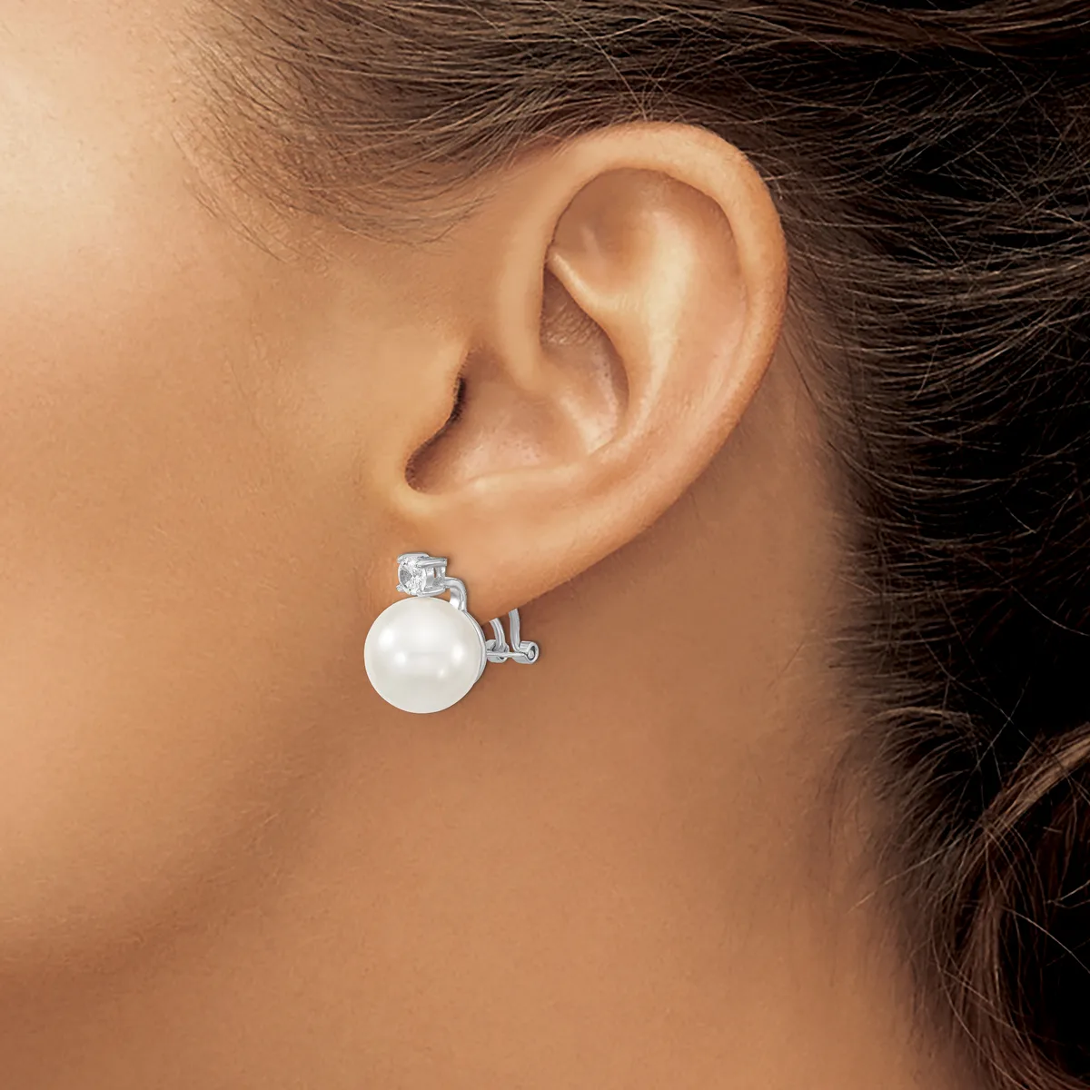 A woman wearing a silver earring with a white pearl and small rectangular stone stud, shown from the side view near her ear.