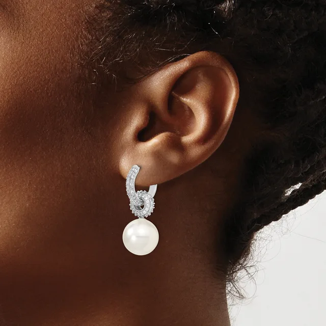 A person wearing a silver hoop earring with a dangling white pearl, shown from the side against their ear.