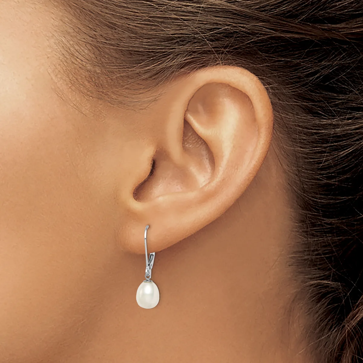 A woman wearing a silver drop earring with a white pearl pendant hangs from her earlobe.