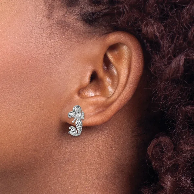 A silver seahorse-shaped earring worn on a person's earlobe, featuring a polished finish and small stamped hallmark.
