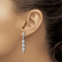 A woman wearing a long dangling earring made of polished silver spheres connected in a vertical line, shown from the side view of her ear and neck.