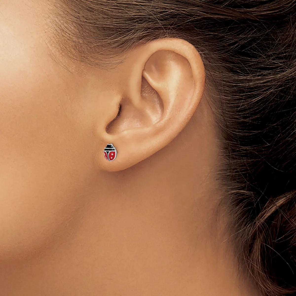 A close-up view of a person's ear wearing a small red and black ladybug-shaped stud earring.