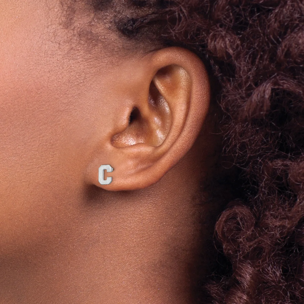 A person wearing a single silver letter C stud earring in their earlobe, shown in profile against their neck and shoulder.