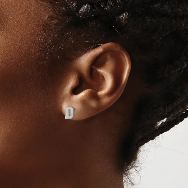 A person wearing a small silver letter D stud earring on their earlobe.