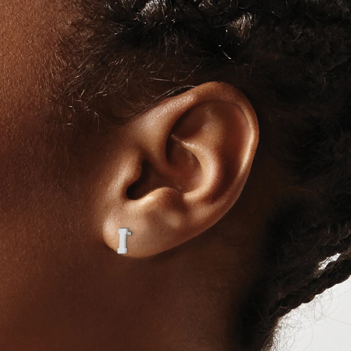 A small rectangular silver earring worn in a pierced earlobe, shown from the side on a person with brown skin and dark hair.