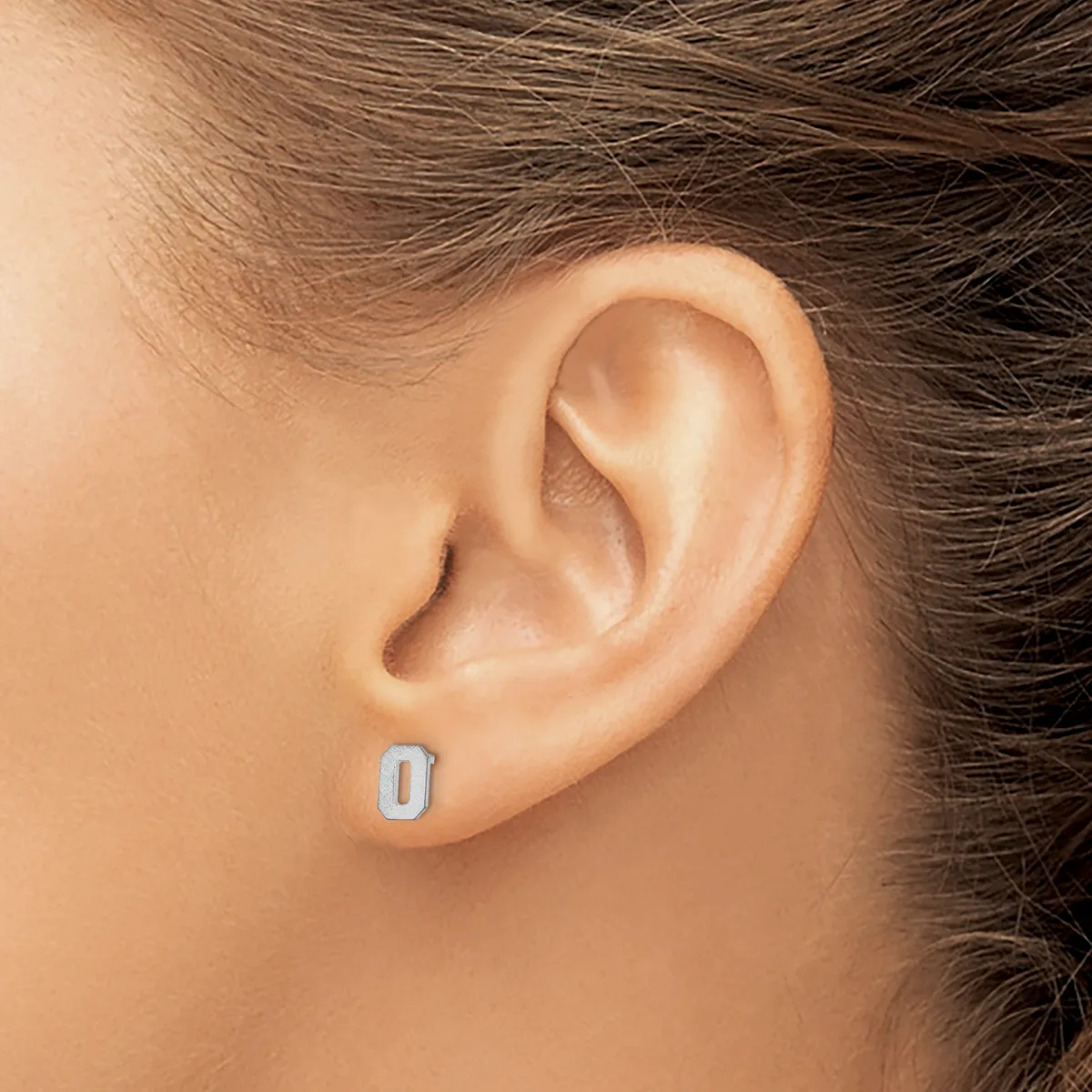 A person wearing a small rectangular silver stud earring in their earlobe, shown in profile against their neck and shoulder.