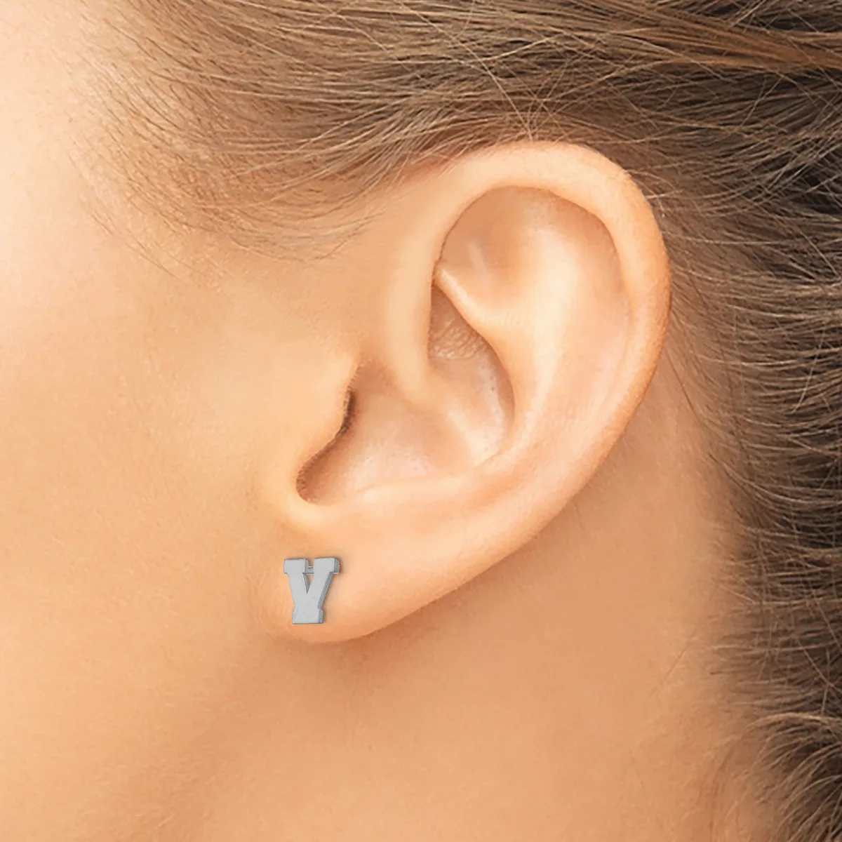 A small rectangular blue-grey stud earring worn in a pierced earlobe on a person with brown hair.