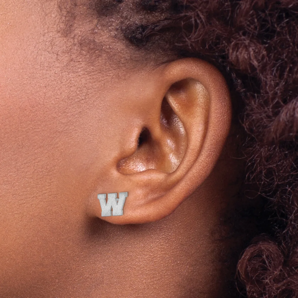 A person wearing a silver stud earring in the shape of the letter W on their earlobe.