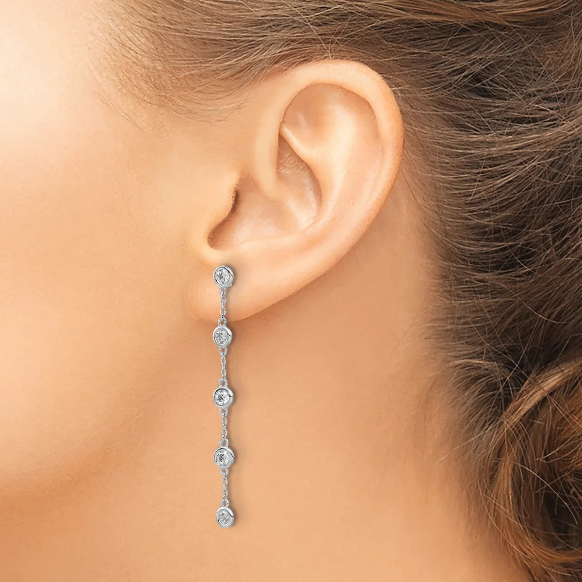 A woman wearing a long dangling earring with five round diamond-shaped stones connected by thin silver links.