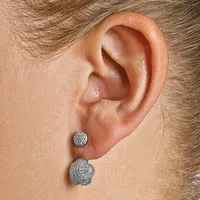 A person wearing two diamond-encrusted earrings on their earlobe, one smaller round stud and one larger flower-shaped design.